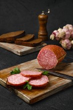 Smoked beef salami and sandwich on cutting board over black background