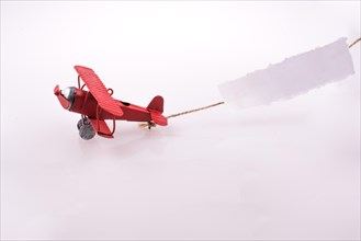 Red plane flying with a paper after it on a white background