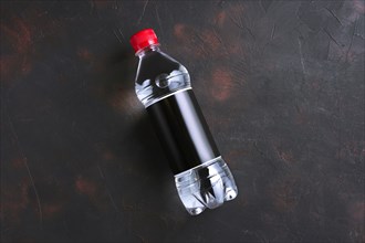 Plastic bottle of water with black label and red cap on table