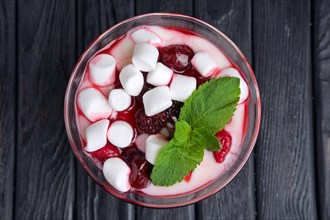 A glass of youghurt with marshmallow and raspberries decorated with mint leaves. Top view