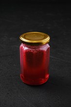 Whole closed jar of cherry jam on black background