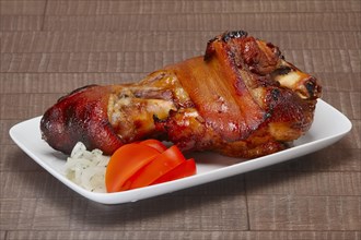Baked pork shank with fresh slices of onion and tomato on wooden table