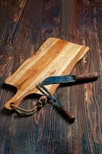 Shabby wooden table with empty cutting board and old forged knife and fork for barbecue