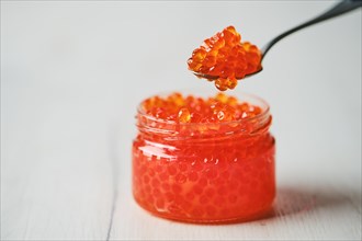 Photo with shallow depth of field of open jar with red caviar and a spoon above it