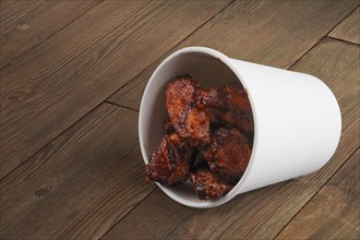 Cardboard container with fried chicken wings laying on wooden floor