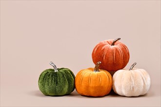 Multi colored pumpkin decoration made from velvet fabric in corner of beige background with copy space