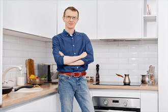 Smiling mid adult man stands in the kitchen with his arms crossed