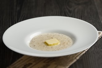 Plate of liquid oatmeal with melting piece of butter on wooden table