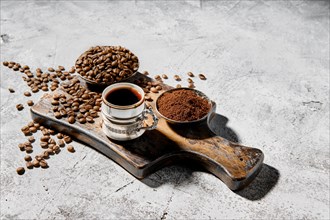 Hot cup of espresso with coffee beans scattered on wooden board and a pot under hard morning sun