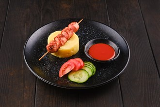 Fried sausage on skewer with mashed potato and slices of fresh tomato and cucumber