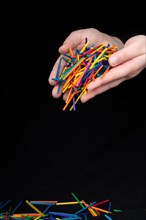Hand letting coloured wooden sticks fall on black background