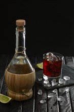 Bottle of homemade vodka and cold cocktail with lime and coffee liquor on dark background