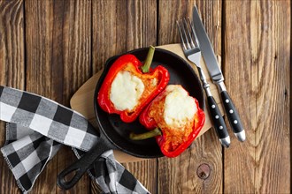 Bell pepper stuffed with meat with melted cheese mozzarella on top baked in oven in cast iron skillet. Top view. Natural wooden background