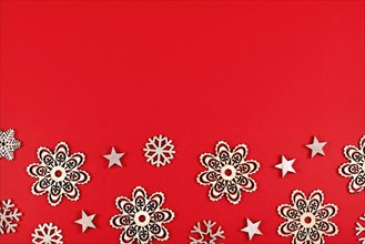 Christmas flat lay with wooden snowflake and star ornaments at bottom of red background with empty copy space