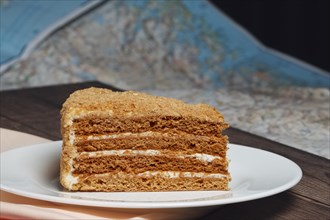 Piece of honey cake on plate near map on the table