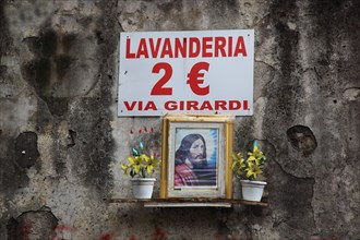 Advertising sign of a laundry in combination with an image of a saint on a wall in the old town of Naples