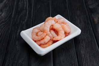 Small boiled peeled shrimps in small plate on dark wooden background