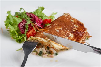 Cutting with knife omelet with ham and fresh vegetables