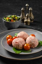Semifinished frozen veal meatballs on a plate with basil and tomato