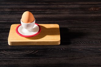 Egg cup with brown egg on wooden table and harsh shadow