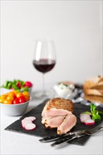 Sliced grilled pork fillet with fresh tomatoes and raddish served with glass of red wine. Soft focus photo