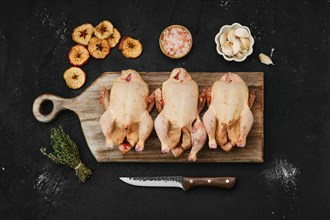 Overhead view of three little raw chicken on wooden cutting board