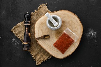 Wooden cross section with paprika in plastic package and stone mortar and mill