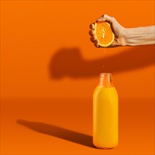 Hand squeezing orange juice in bottle on bright background. Hard light and harsh shadows
