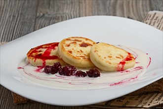 Pancakes with sower cream and cherry syrup on wooden table