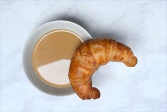 Coffee with milk in bowl and croissant