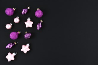 Modern seasonal Christmas flat lay with pink and bright violet glittering tree bauble ornaments on left side and empty dark black copy space on right side