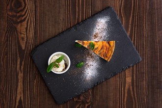 Top view of layered cheesecake with ice cream served on slate plate on dark wooden background