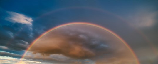Double rainbow in atmospheric sky with thunderclouds at sunset