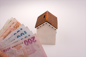 Turkish Lira banknotes by the side of a model house on white background