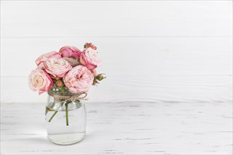Pink roses flower glass jar white wooden textured backdrop