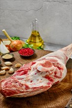 Raw whole lamb leg chump on with ingredients on wooden stump closeup