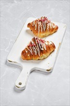 Fresh croissant with raspberry jam on white wooden board on marble background