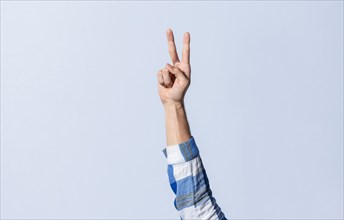 Hand gesturing the letter V in sign language on an isolated background. Man's hand gesturing the letter V of the alphabet isolated. Letter V of the alphabet in sign language