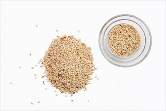 Top view of sesame seeds in a little dish and spilled on white background