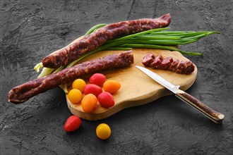 Dried beef sausage on wooden cutting board with spring onion and tomato