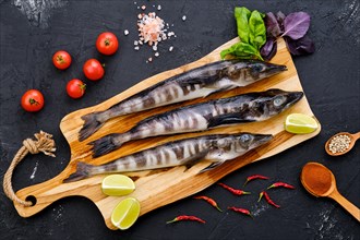 Top view of raw fresh icefish on wooden cutting board with spice and herbs