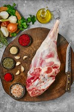 Raw whole lamb leg chump on with ingredients on wooden stump