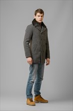 Full length portrait of handsome man in warm woolen coat posing in studio
