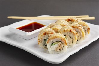 Closeup view of chicken teriyaki roll with chopsticks and soy sauce on a plate