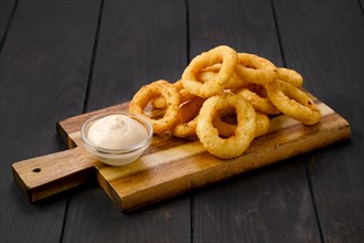 Deep fried breaded squid rings with creamy sauce on wooden serving board