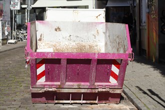 Pink skip for building rubble standing on the road