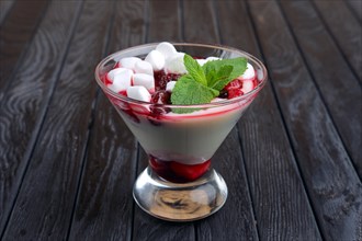 A glass of youghurt with marshmallow and raspberries decorated with mint leaves