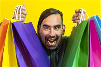 Close-up of a crazy man holding colorful shopping bags over yellow background