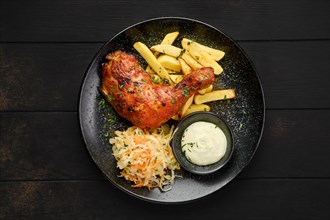 Top view of baked chicken leg with american fries and pickled cabbage on a plate