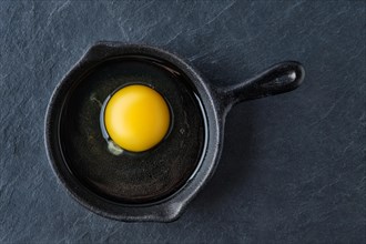Top view of raw uncooked egg in small cast-iron skillet
